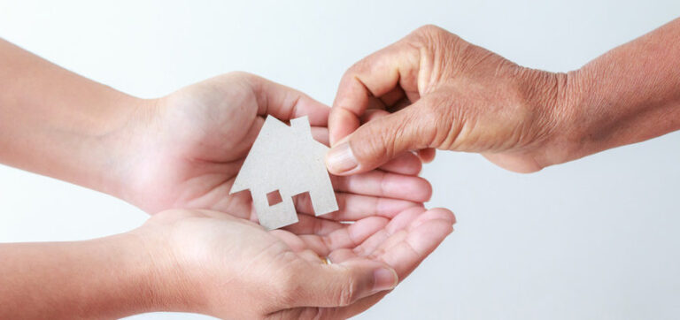 Hand of old women giving paper card house to young woman metaphor and concept for asset heritage of mother and daughter
